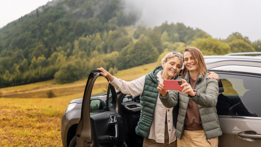 Zwei Frauen machen ein Selfie vor einem Auto.