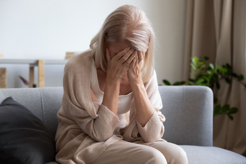 Eine Frau sitzt auf einem Sofa und schlägt die Hände vors Gesicht.