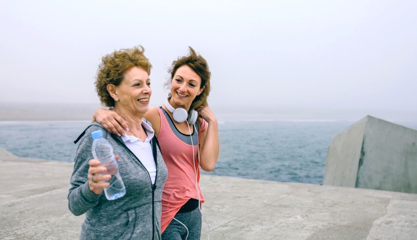 Zwei Frauen in Sportkleidung gehen Arm in Arm am Meer entlang