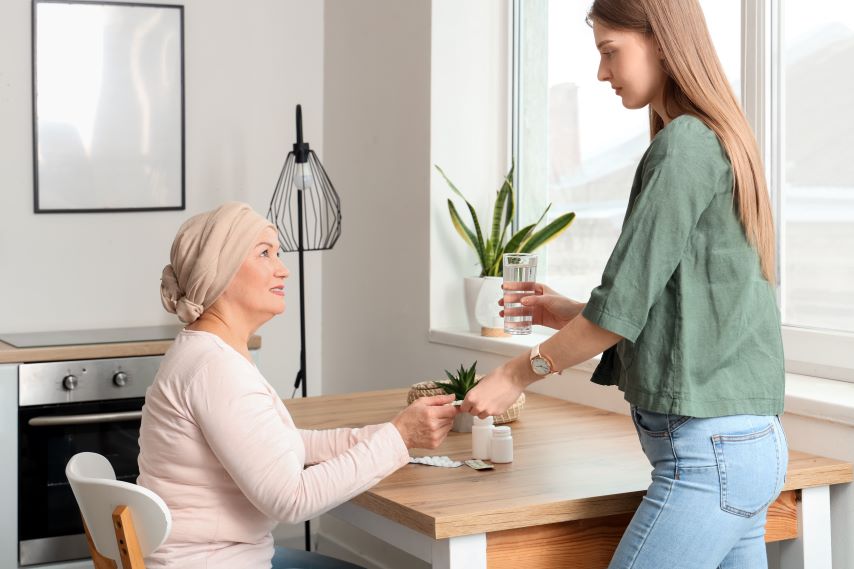 Eine Frau sitzt an einem Tisch, eine jüngere Frau reicht ihr ein Glas.