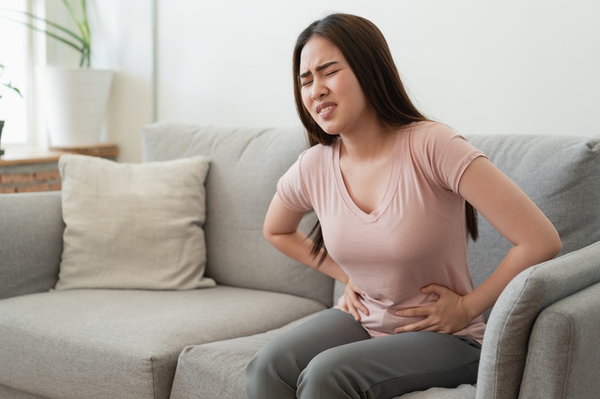 Eine junge Frau sitzt auf einem Sofa und hält sich den schmerzenden Unterleib.